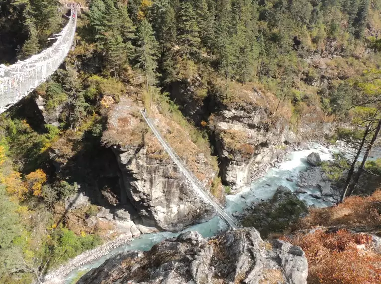 Hängebrücke über einem Fluss, umgeben von Bergen.