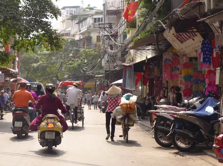 Menschen auf Fahrrädern und Mopeds in einer belebten Straße in Hanoi, Vietnam.