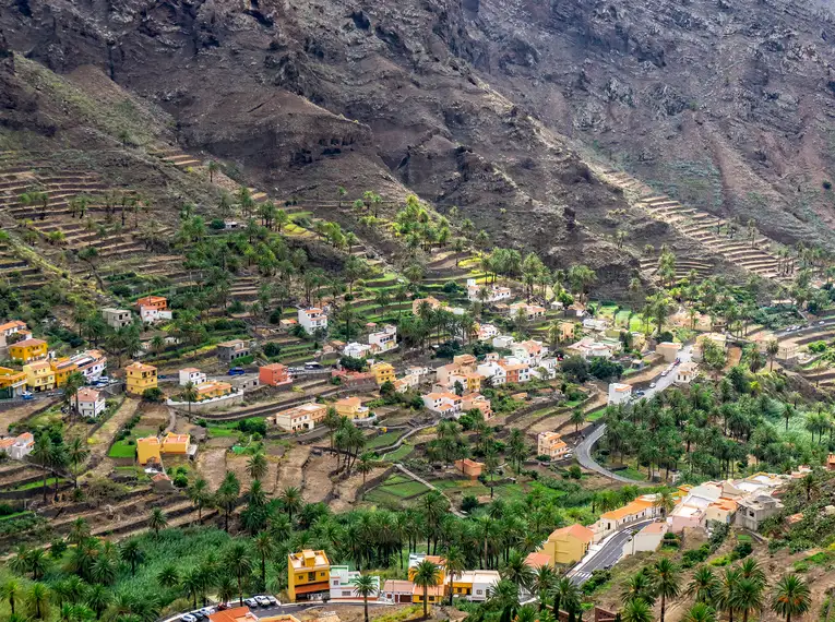 Blick auf ein Dorf in La Gomera mit Bergen im Hintergrund und Palmen im Tal.