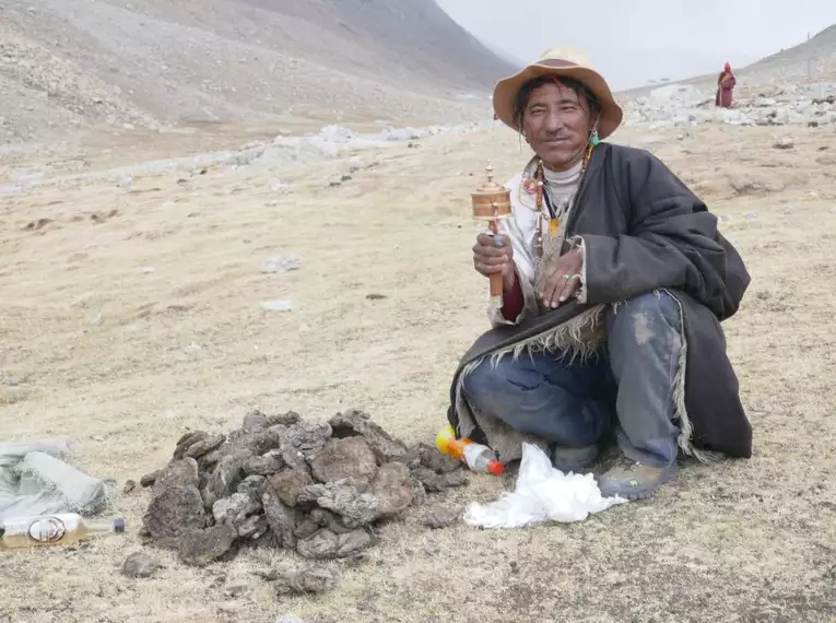 Ein Bergsteiger mit Gebetsmühle und traditioneller Kleidung in der Himalaya-Landschaft Tibets.