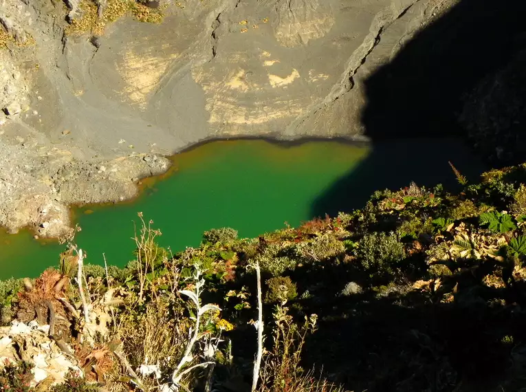 Ein Kratersee mit grünem Wasser, umgeben von Felswänden und Vegetation.
