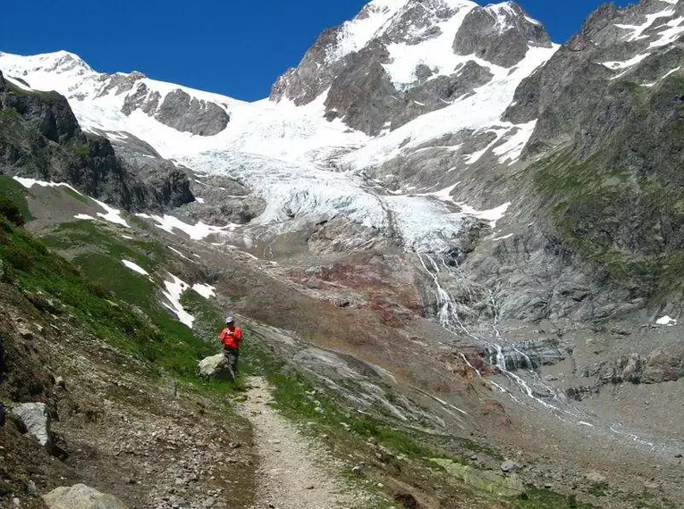 Wanderer auf einem Gebirgspfad mit schneebedeckten Gipfeln in den Alpen.
