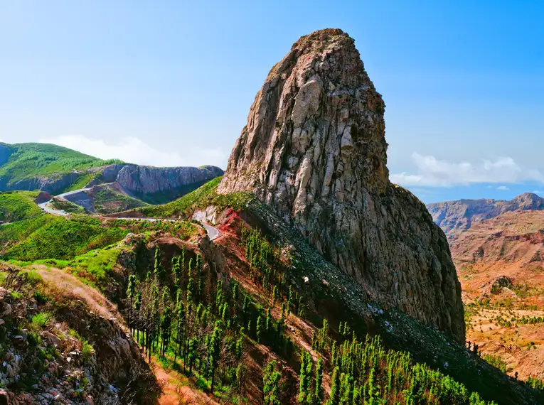 Blick auf den imposanten Roque Agando auf La Gomera, umgeben von grüner Vegetation und blauem Himmel.