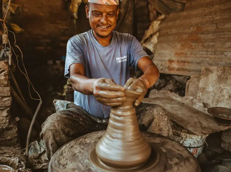 Ein lächelnder Mann töpfert in einer traditionellen Werkstatt in Nepal.