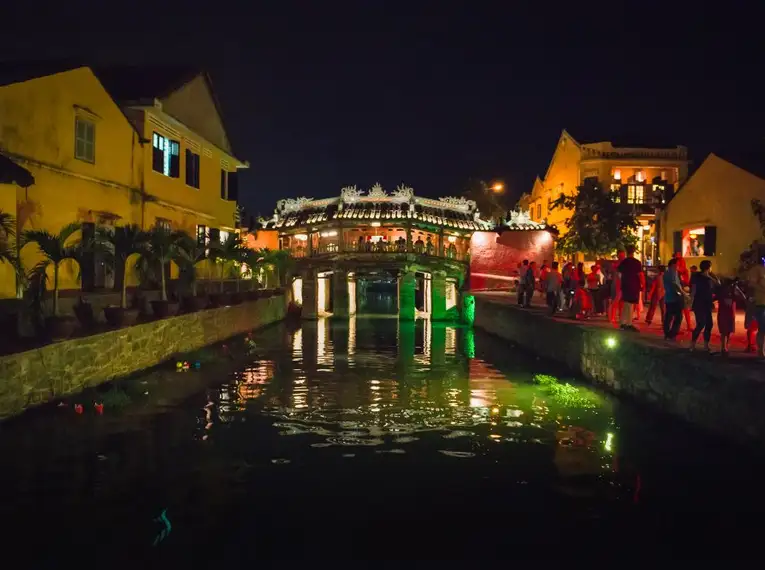 Stimmungsvolle Beleuchtung und Menschen an einer Brücke in Hoi An bei Nacht.