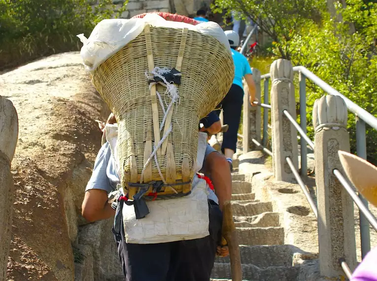 Träger in Chinas Bergregionen Einheimischer Träger trägt Waren auf einer steinigen Treppe in einer Bergregion in China.