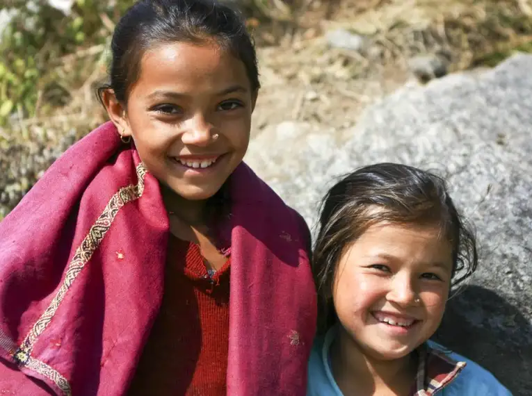 Zwei lächelnde Kinder in traditioneller Kleidung in einer Berglandschaft.