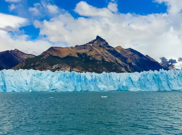 Perito Moreno Gletscher - was für eine tolle Farbe! Blau schimmernder Gletscher vor steilem Berg unter blauem Himmel in Patagonien.