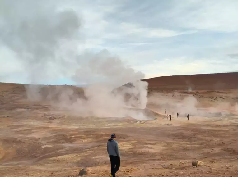 Personen beobachten dampfende Geysire in der Atacama-Wüste.