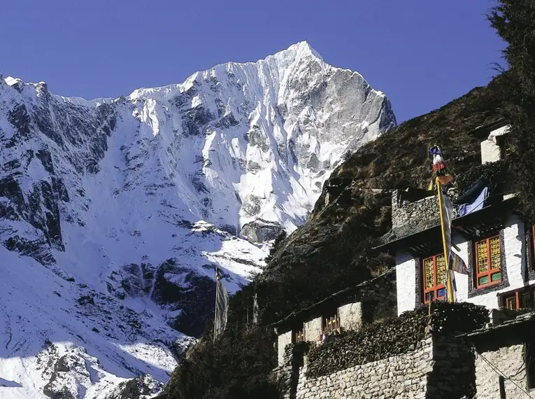Verschneite Berge in Nepal, traditionelles Haus im Vordergrund.