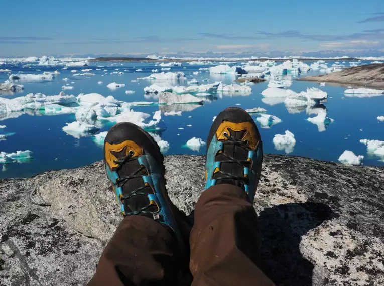 Einfach mal die Seele baumeln lassen und die Aussicht genießen Person mit Wanderstiefeln entspannt mit Blick auf Eisberge in Grönland.