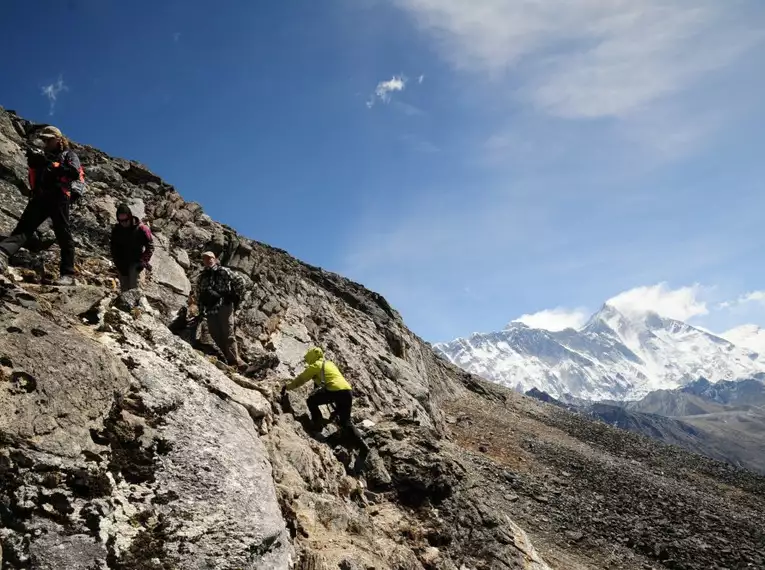 Wanderer auf felsigem Pfad mit schneebedeckten Bergen im Hintergrund.