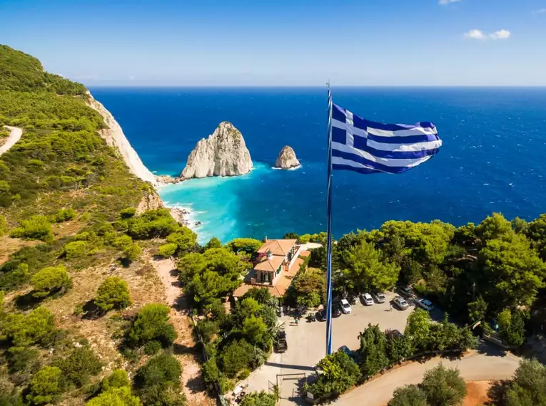 Atemberaubendes Panorama während unserer Wanderungen Griechische Flagge weht über der Küste von Zakynthos mit blauem Meer und weißen Felsen.