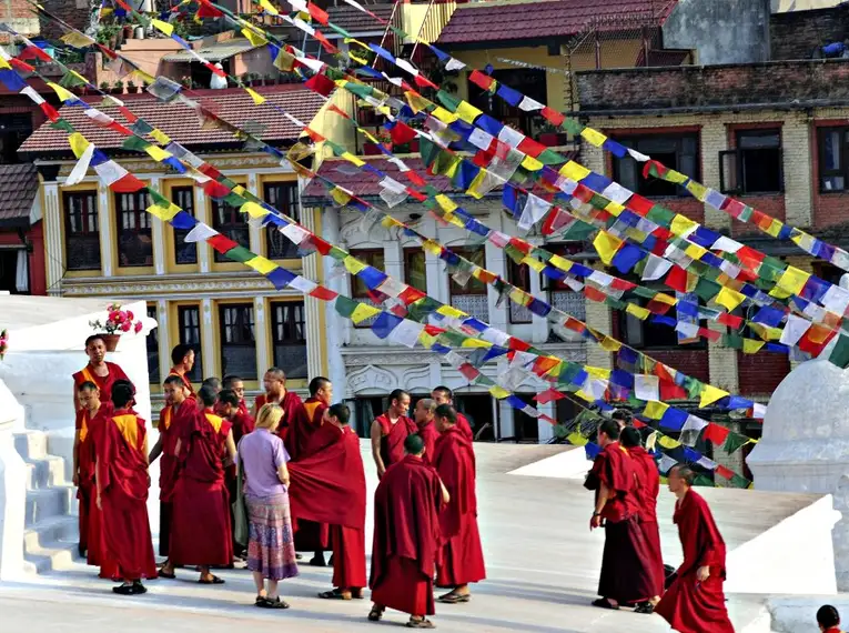 Mönche in roten Roben vor einem Stupa mit bunten Gebetsfahnen in Nepal.