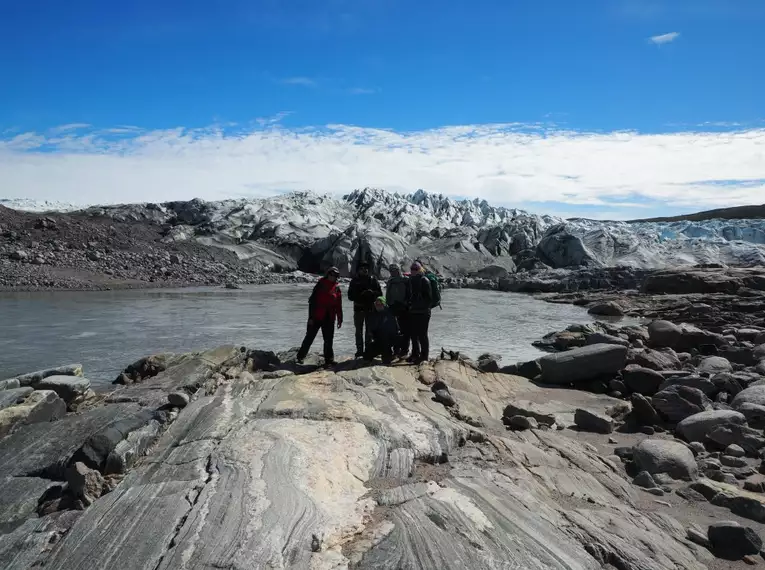 Wanderung in Grönlands arktischer Landschaft Gruppe von Wanderern vor einem Gletscher in Grönland mit felsigem Gelände und blauem Himmel.