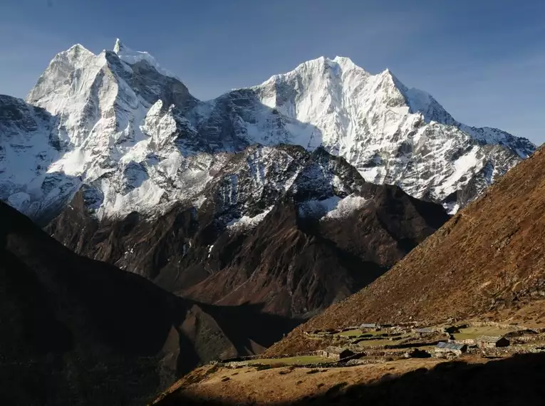 Verschneite Himalaya-Berge in Nepal mit Blick auf ein Dorf im Vordergrund.