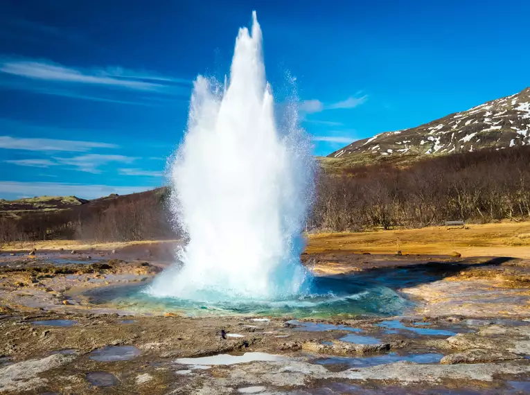 Geysir-Ausbruch in Island Ein beeindruckender Geysir-Ausbruch in Islands Landschaft, umgeben von Bergen.