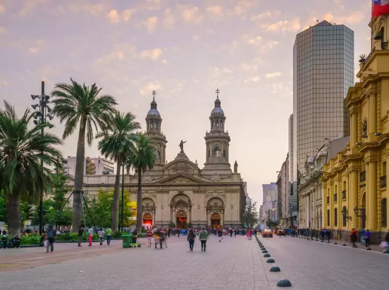Eine belebte Straße in Santiago de Chile bei Sonnenuntergang, mit historischen und modernen Gebäuden im Hintergrund.