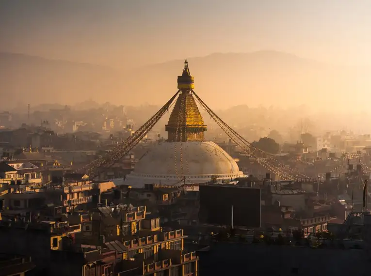 Die Boudhanath-Stupa bei Sonnenuntergang umgeben von Gebäuden.