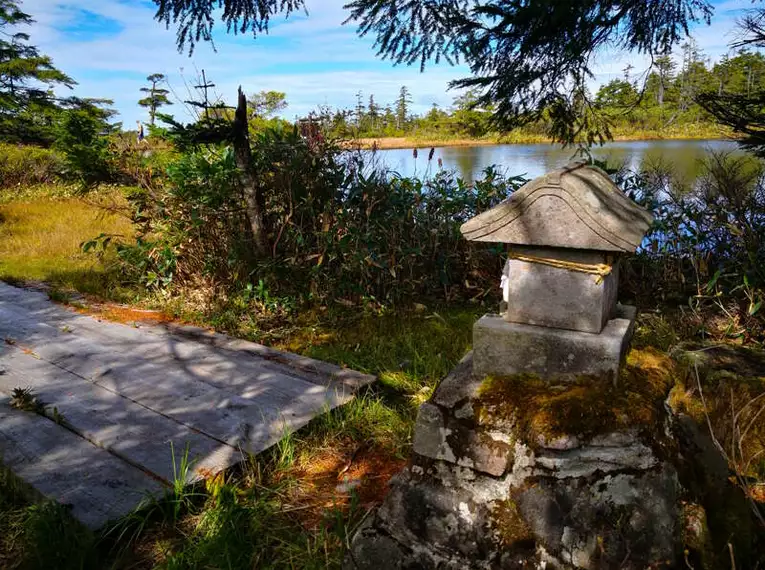 Wandern im Shiga-Naturpark Ein kleiner Stein-Schrein im Shiga-Naturpark, umgeben von herbstlicher Vegetation.