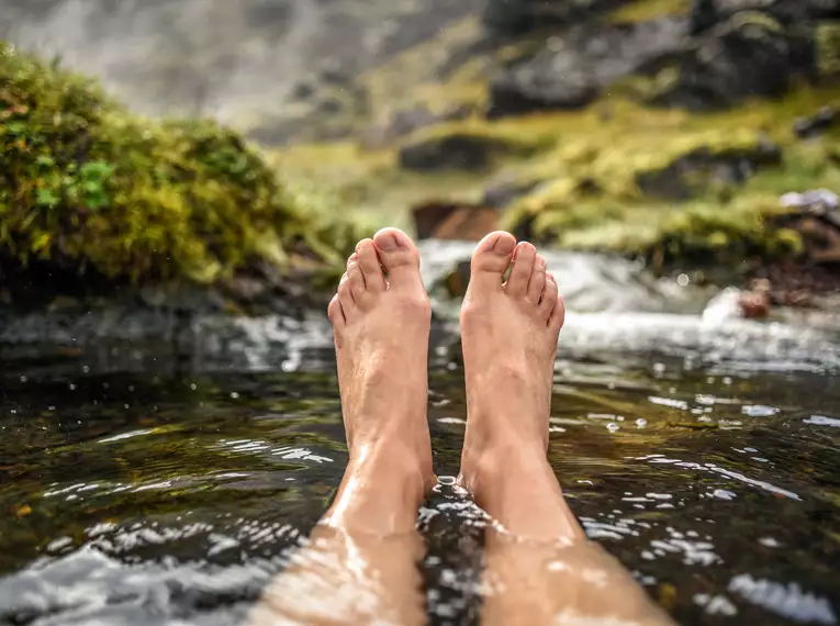 Entspannung in heißen Quellen Person entspannt mit Füßen in einem heißen Fluss, umgeben von Natur in Island.