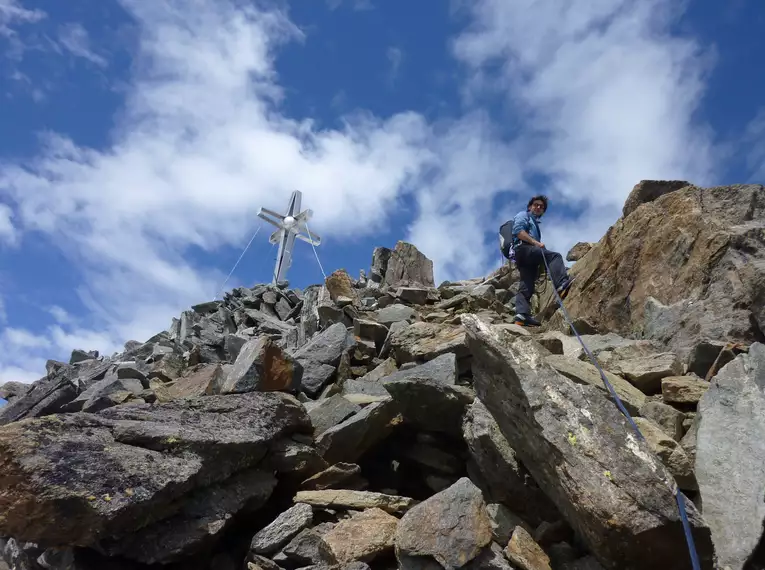 Ein Bergsteiger erklimmt den felsigen Gipfel des Zuckerhütl unter blauem Himmel.