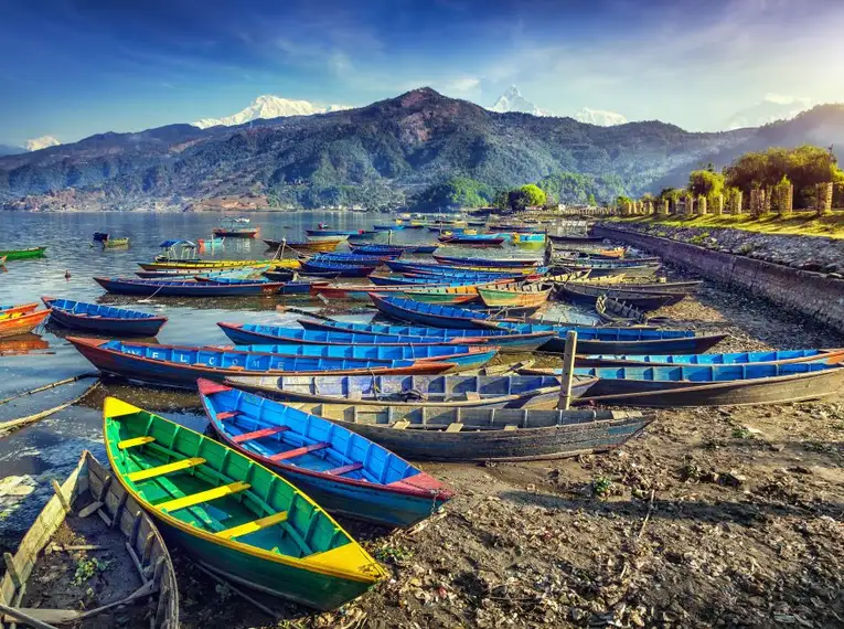 Farbenfrohe Boote am Ufer des Phewa-Sees mit Himalaya im Hintergrund