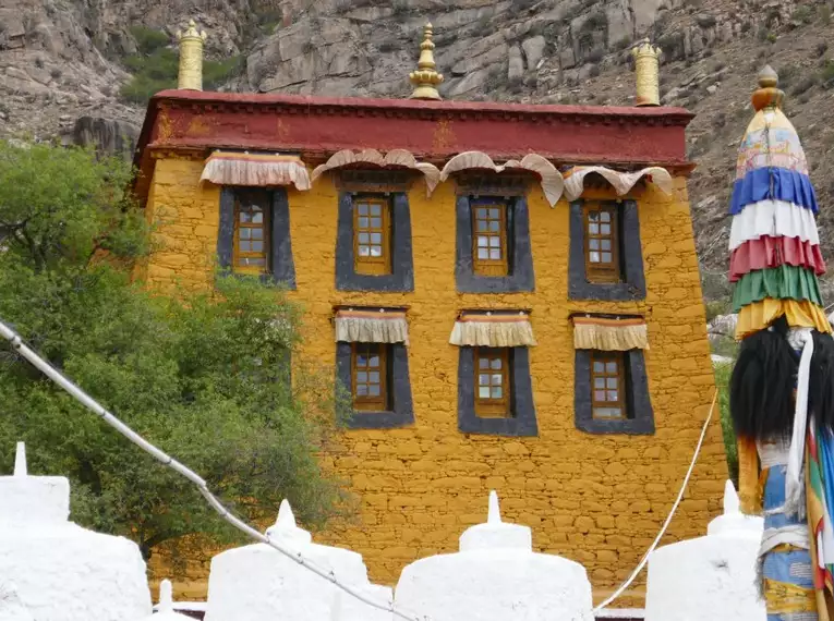 Ein gelbes tibetisches Klostergebäude mit bunten Verzierungen in einer bergigen Landschaft.