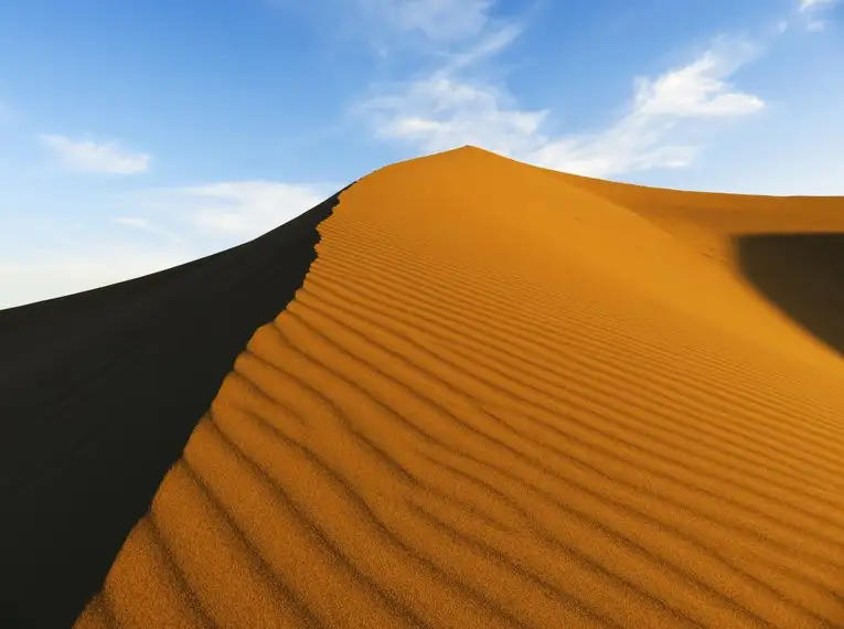 Sanddüne in der Sahara Große Sanddüne in der Sahara mit wellenartiger Struktur und blauem Himmel im Hintergrund.